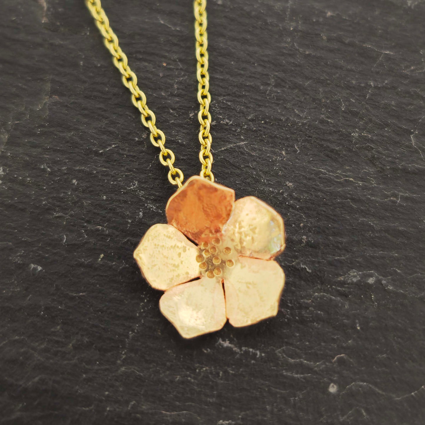 9ct yellow gold flower-shaped pendant necklace on a dark surface.