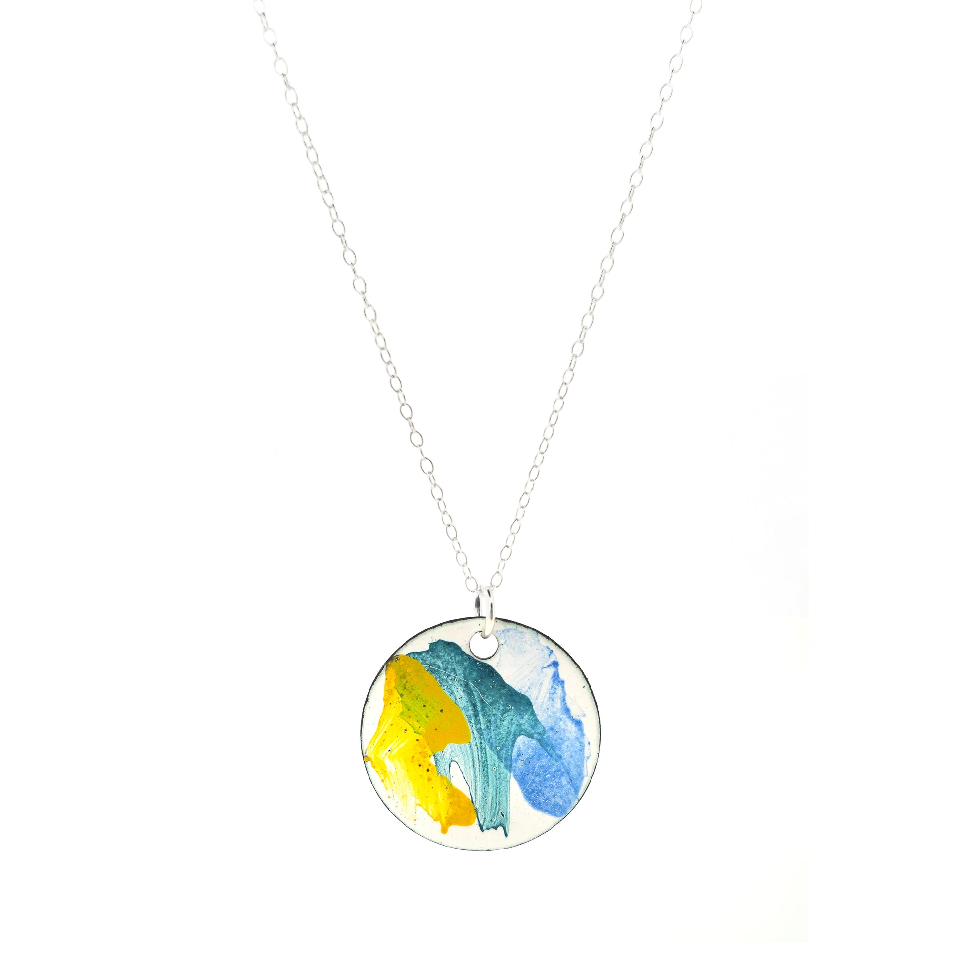 A round enamel pendant with splashes of yellow, green and blue. Suspended on a silver chain.