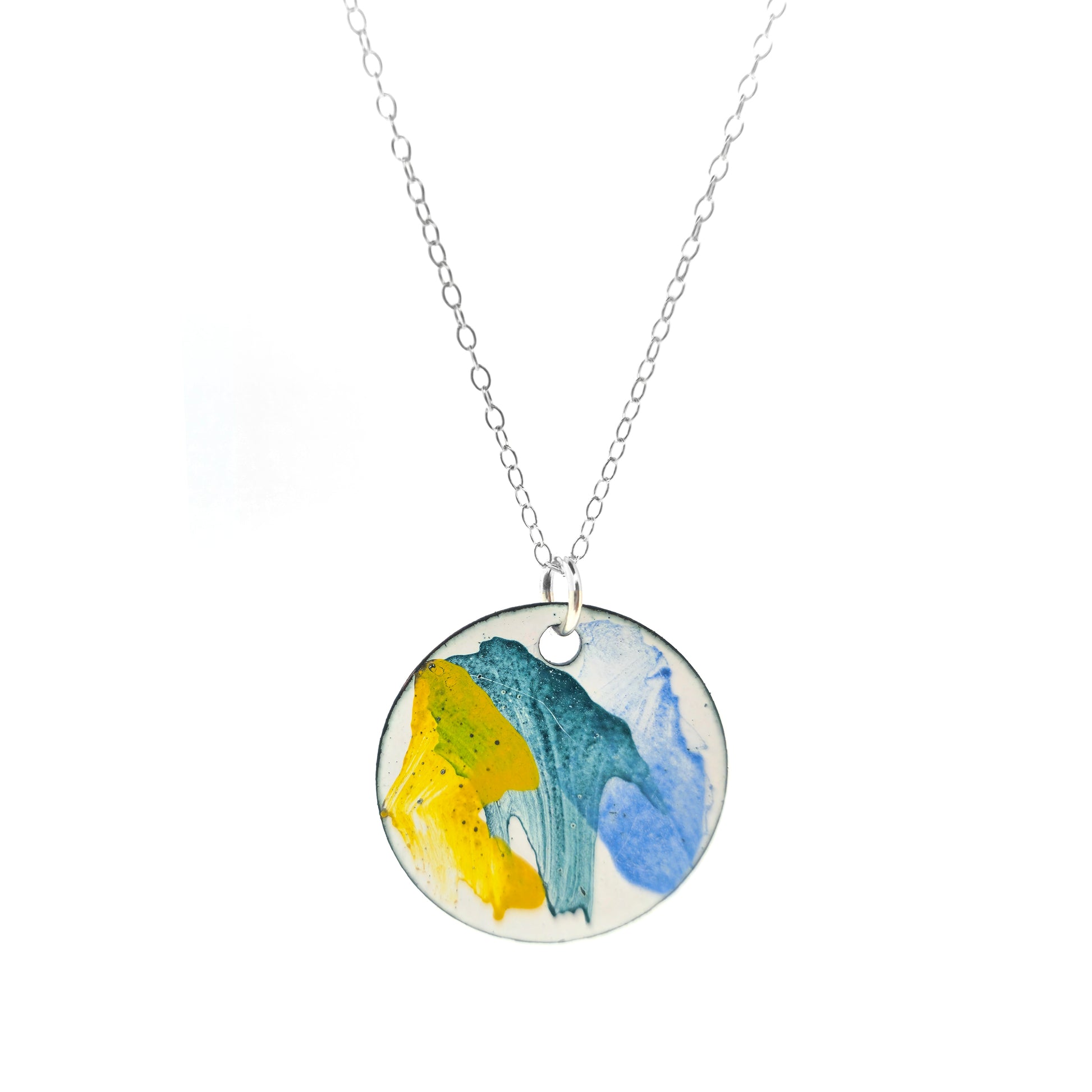 A round enamel pendant with splashes of yellow, green and blue. Suspended on a silver chain.