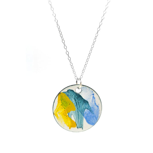 A round enamel pendant with splashes of yellow, green and blue. Suspended on a silver chain.