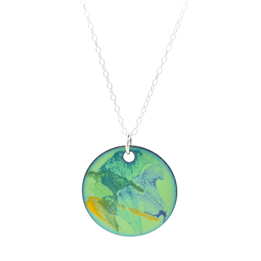 A round enamel pendant with a green background with splashes of dark green, blue and yellow. Suspended on a silver chain.