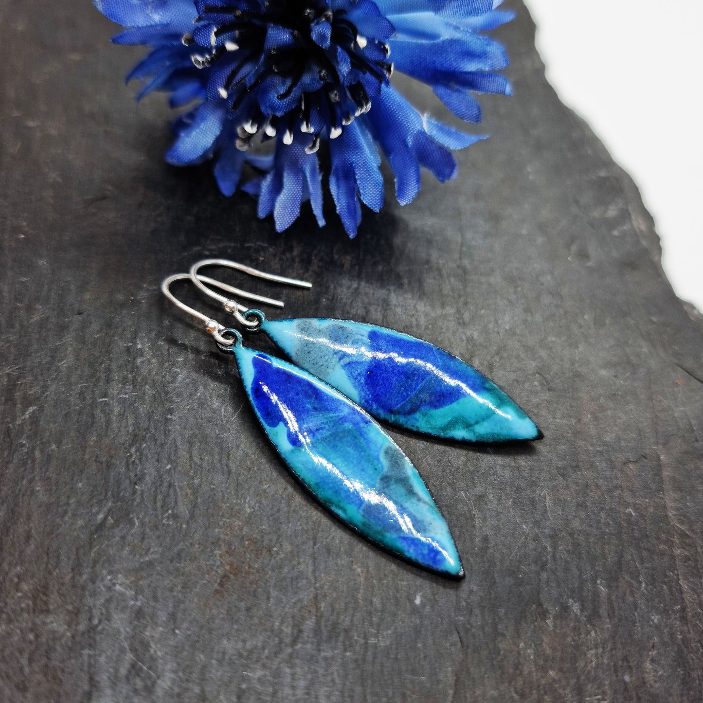 Navette shaped blue enamel drop earrings with splashes of grey and dark blue with flower