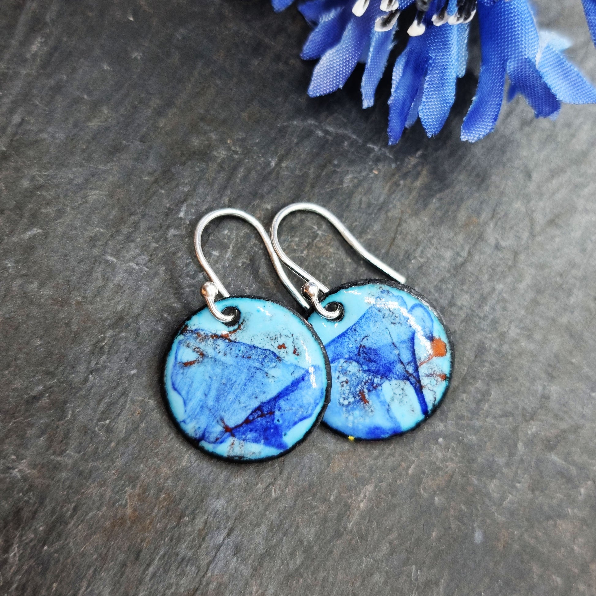 Round enamel drop earrings with splashes of dark blue and red on a light blue background - with flower