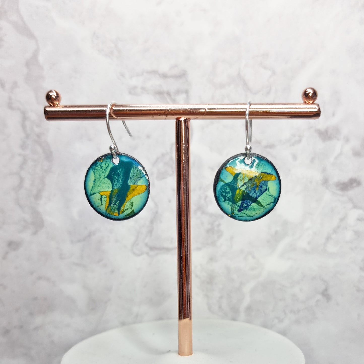 Round enamel drop earrings with splashes of blue, green and yellow on a light green background