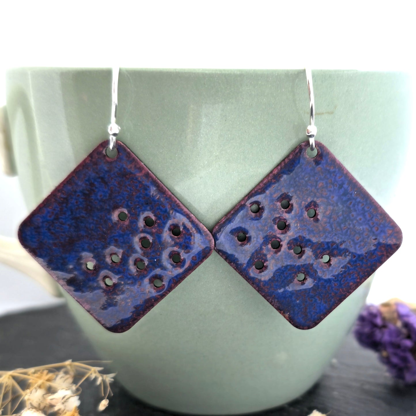 Square blue enamel drop earrings with cut out holes and silver ear hooks on a pale green cup. Handmade. Mijoux Jewellery.