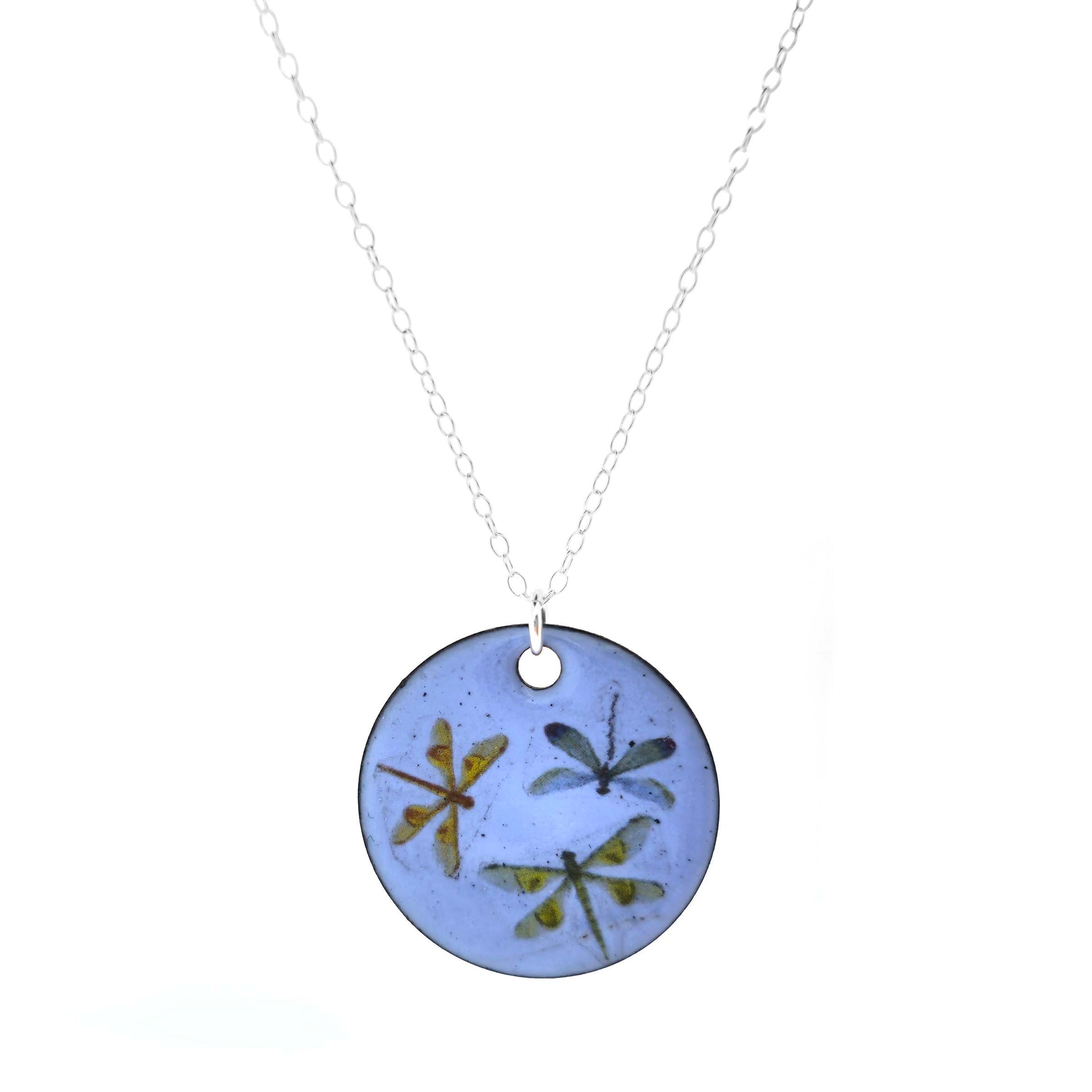 Round enamel pendant with dragonfly designs on a pastel blue background with a silver chain. On a white background.