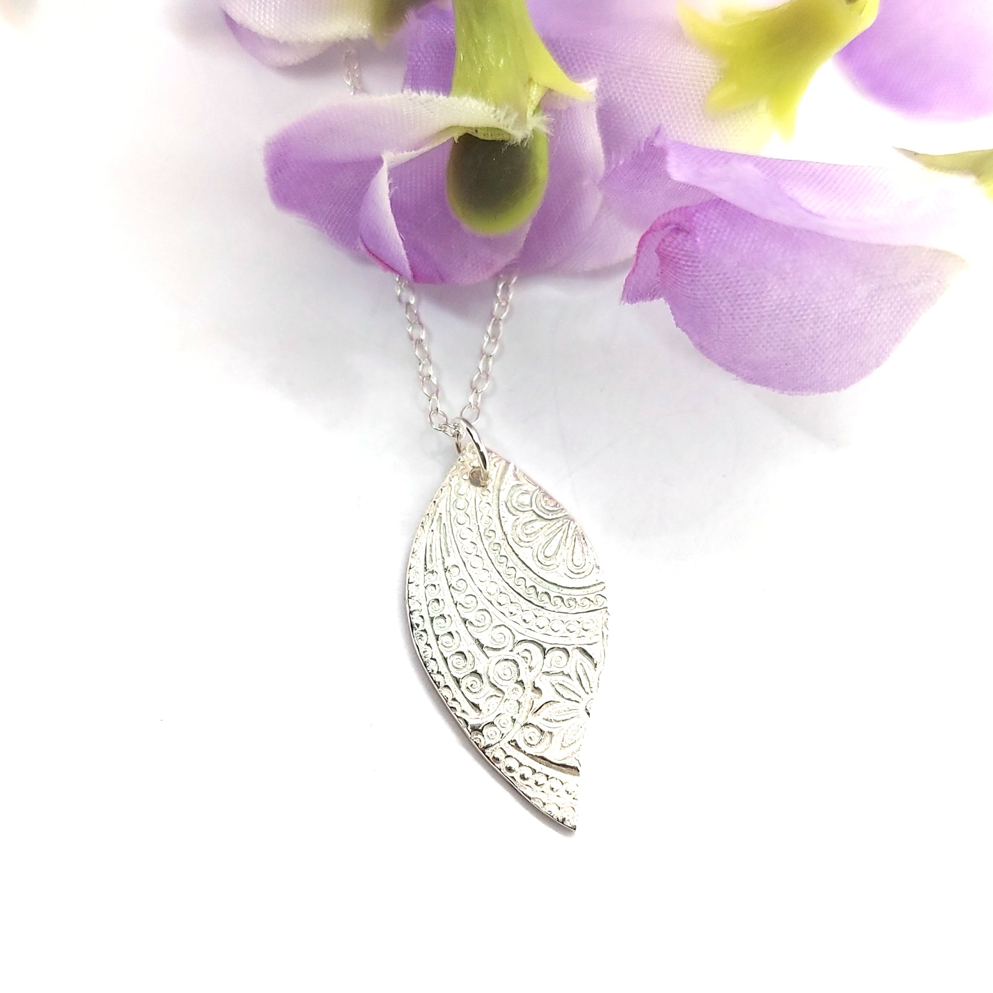 A silver asymmetric patterned leaf-shaped pendant on a chain with flowers