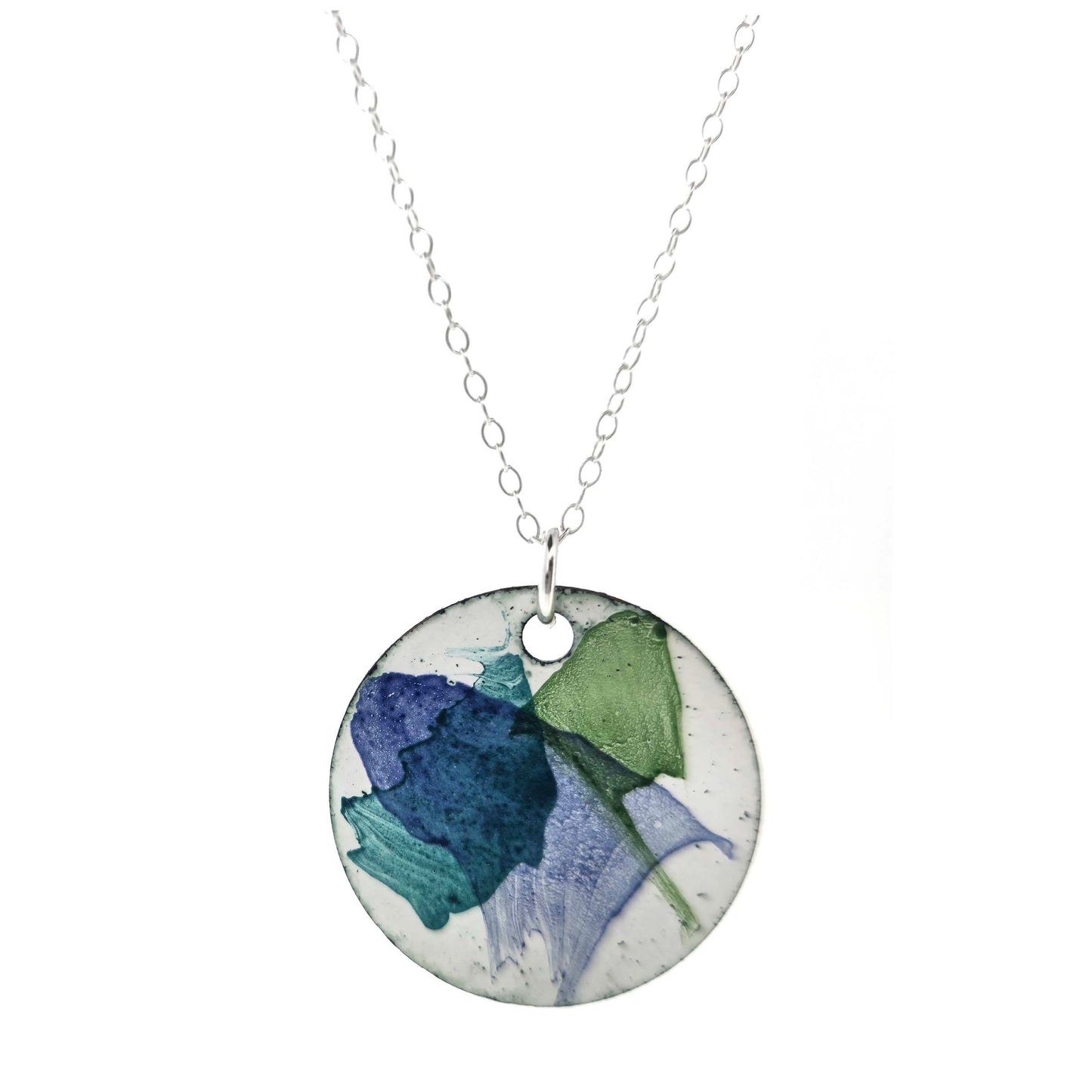 A round enamel pendant with a white background and splashes of dark blue, dark green and jade green. Suspended from a silver chain. Mijoux Creations.