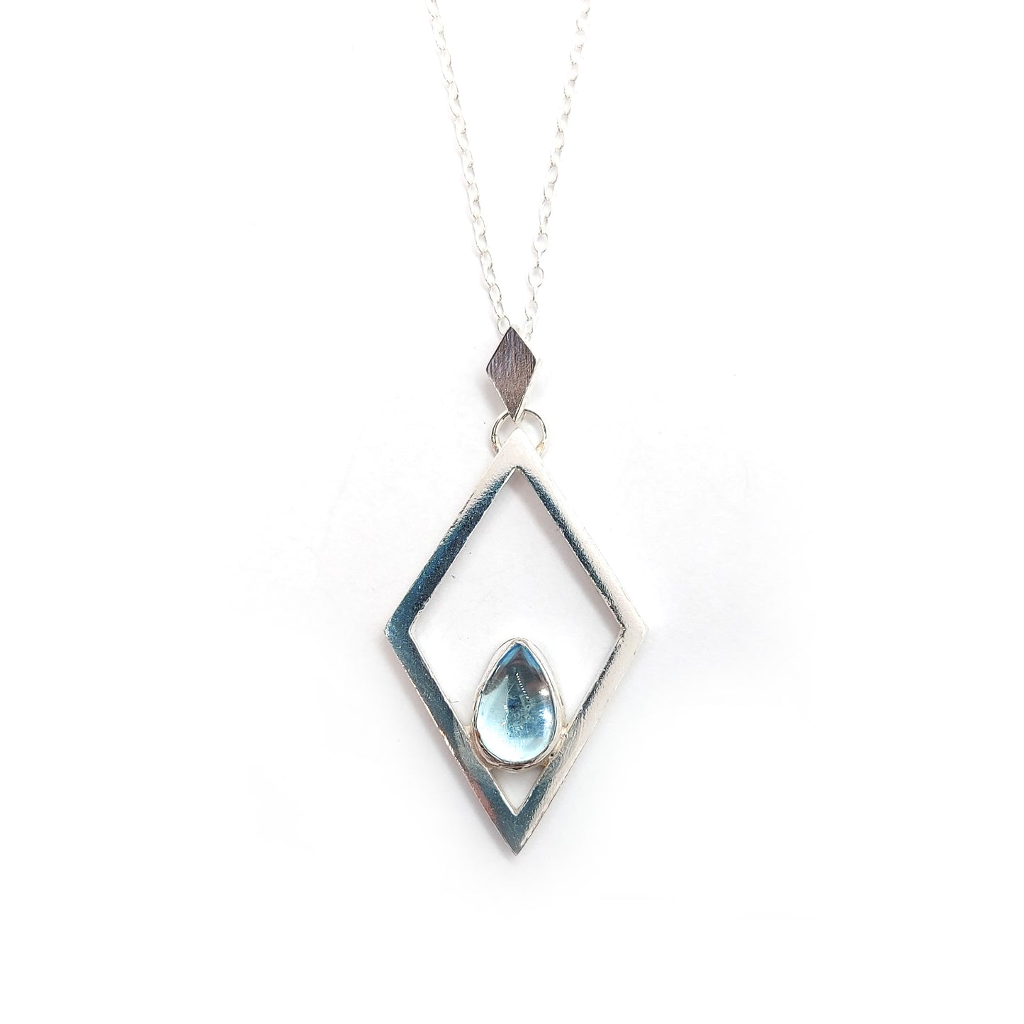 A silver open diamond shaped pendant with a teardrop shaped blue topaz gemstone set inside. A small diamond shaped bail attaches the pendant to a silver chain.