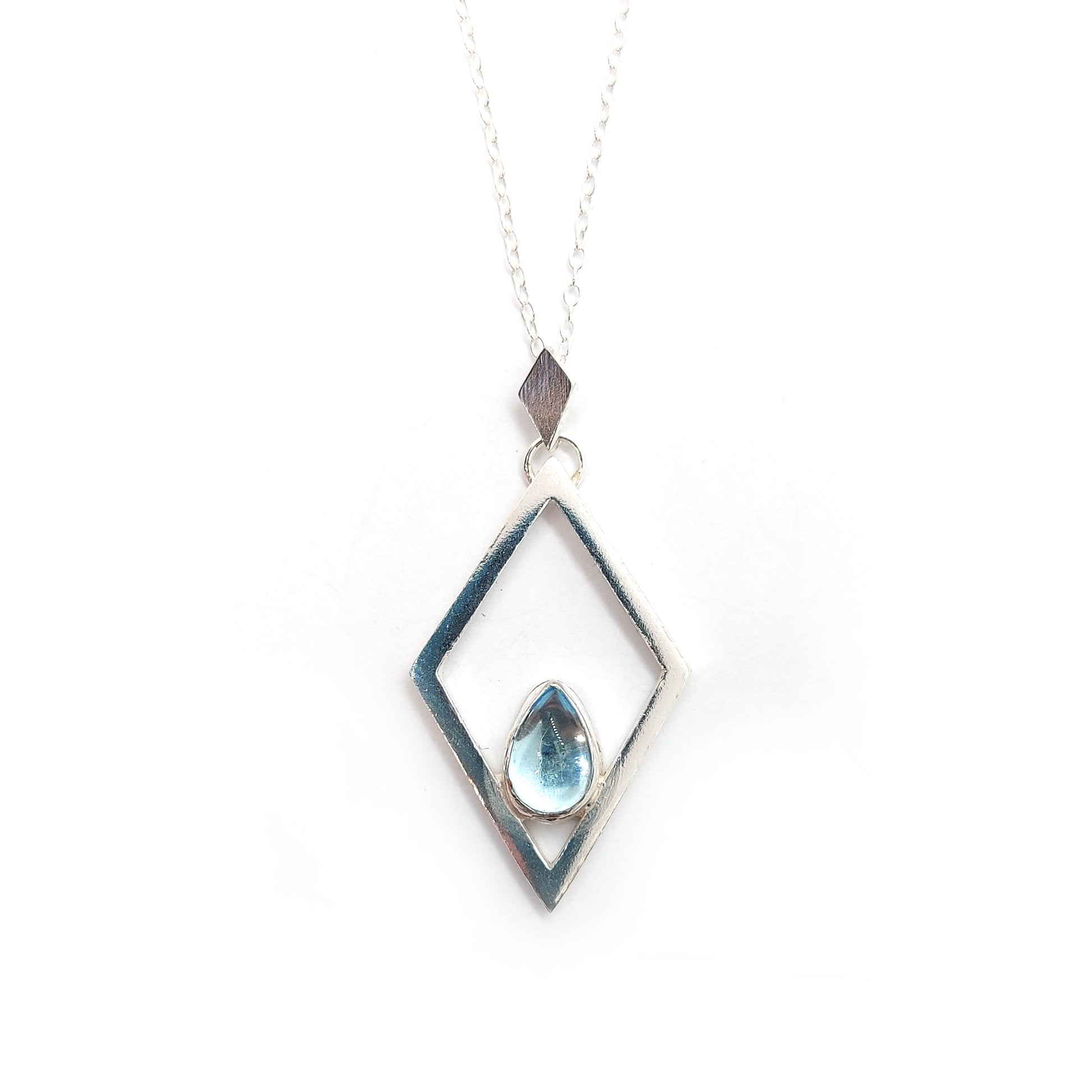 A silver open diamond shaped pendant with a teardrop shaped blue topaz gemstone set inside. A small diamond shaped bail attaches the pendant to a silver chain.