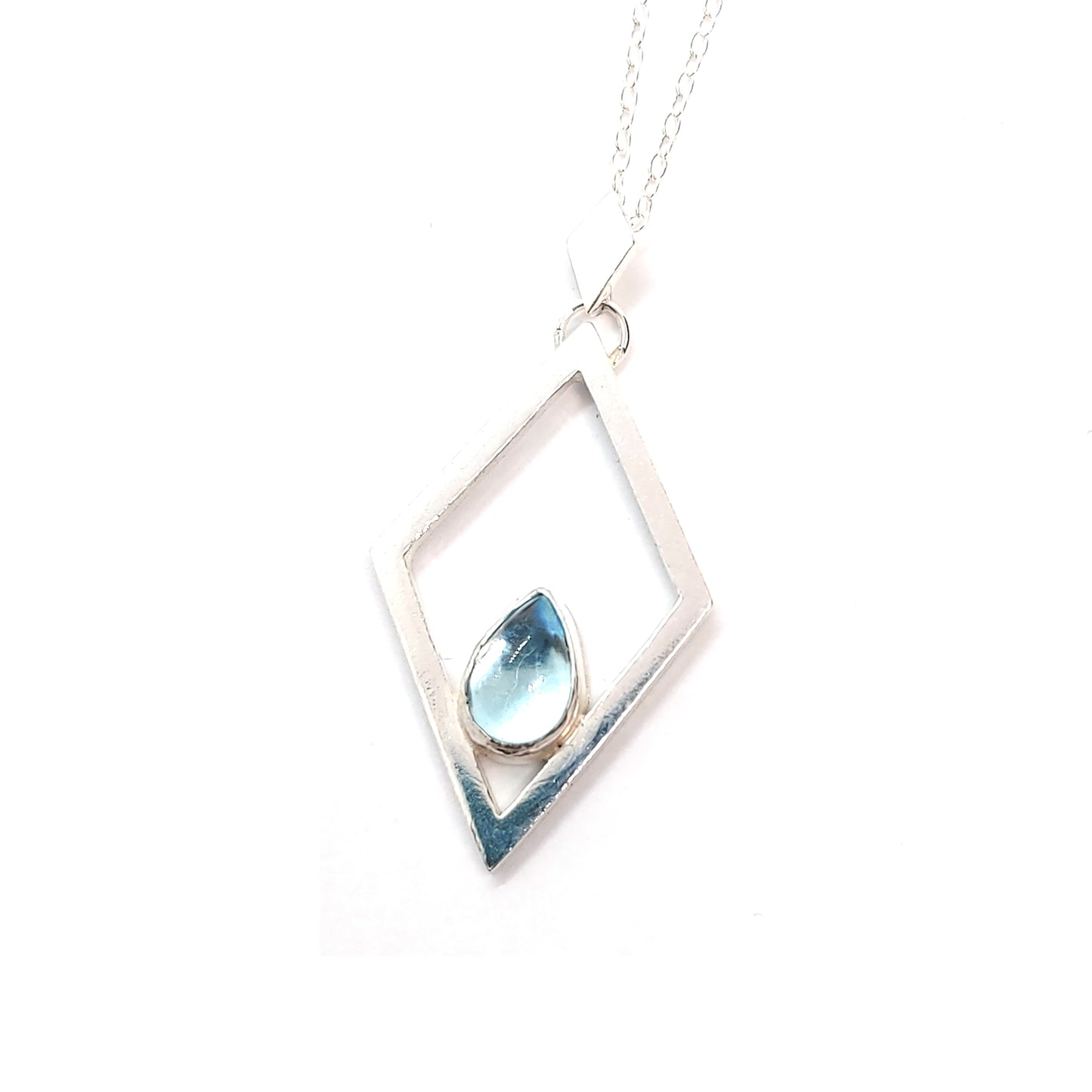 A silver open diamond shaped pendant with a teardrop shaped blue topaz gemstone set inside. A small diamond shaped bail attaches the pendant to a silver chain.