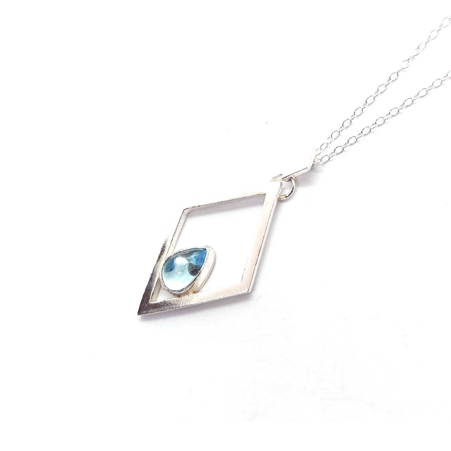 A silver open diamond shaped pendant with a teardrop shaped blue topaz gemstone set inside. A small diamond shaped bail attaches the pendant to a silver chain.