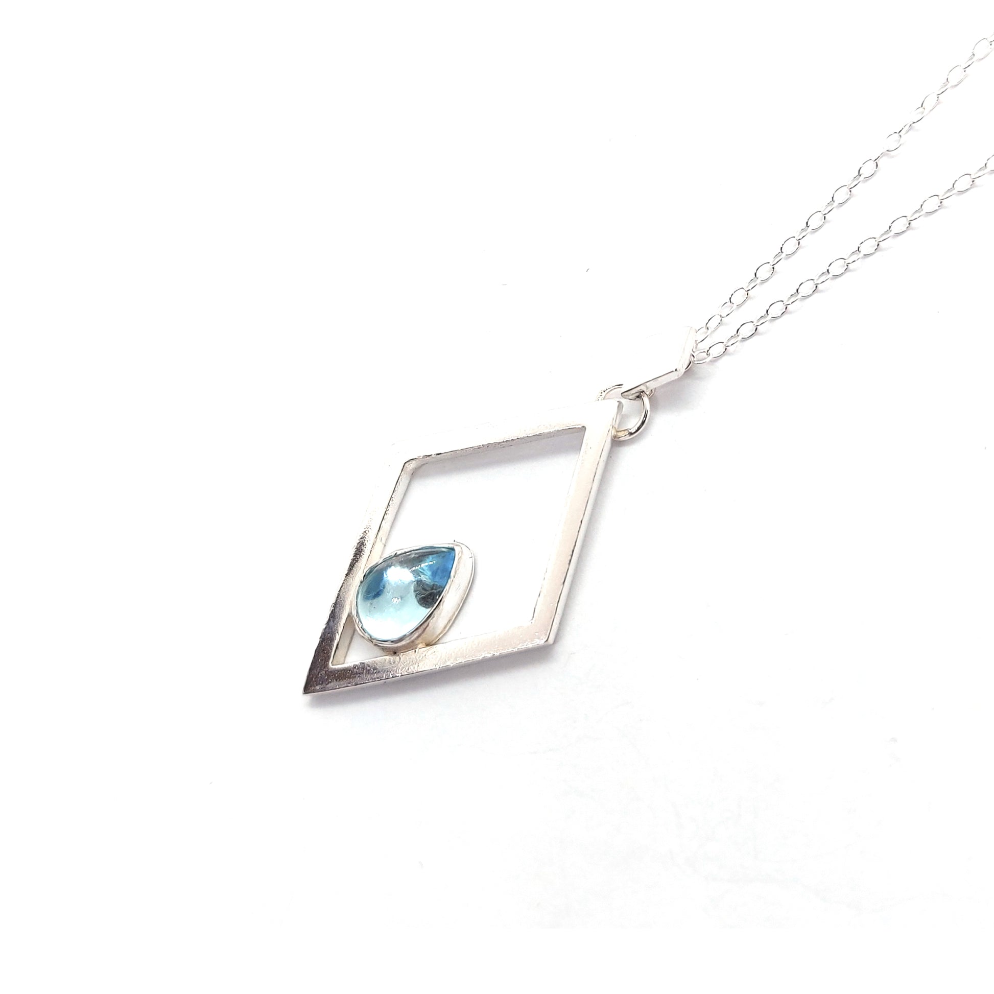 A silver open diamond shaped pendant with a teardrop shaped blue topaz gemstone set inside. A small diamond shaped bail attaches the pendant to a silver chain.