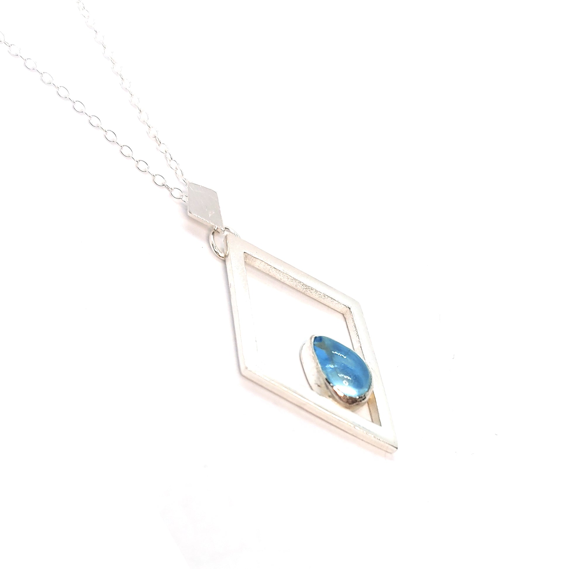 A silver open diamond shaped pendant with a teardrop shaped blue topaz gemstone set inside. A small diamond shaped bail attaches the pendant to a silver chain.