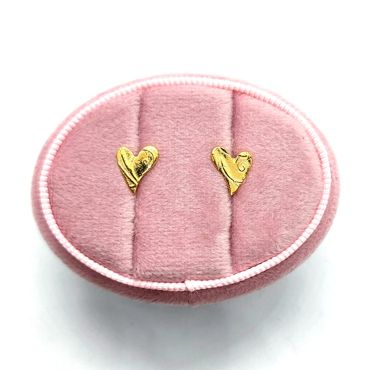 Yellow gold vermeil asymmetrical heart stud earrings with a swirl pattern. Pictured in a pink jewellery box.