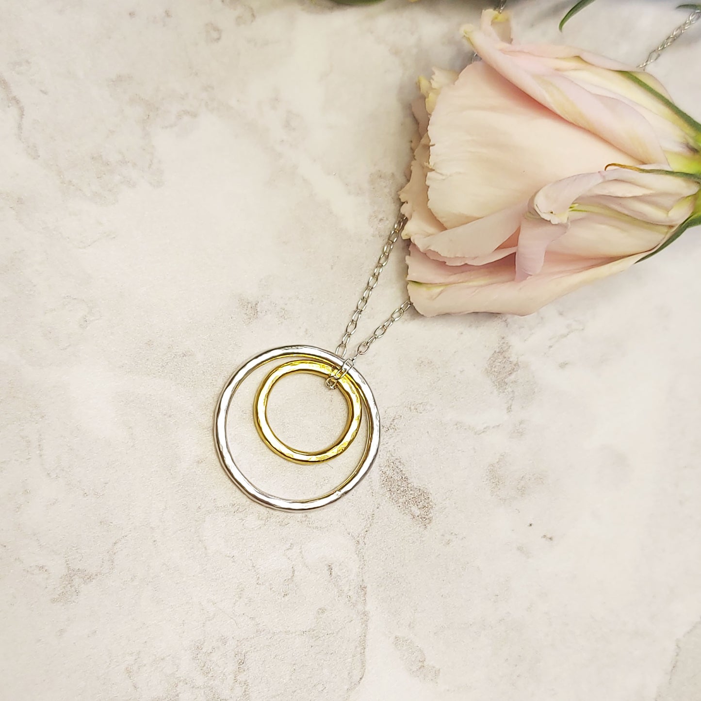 A double circle pendant with an inner yellow gold vermeil hammered circle and an outer silver hammered circle. Suspended on a silver chain. Pictured with a rose.