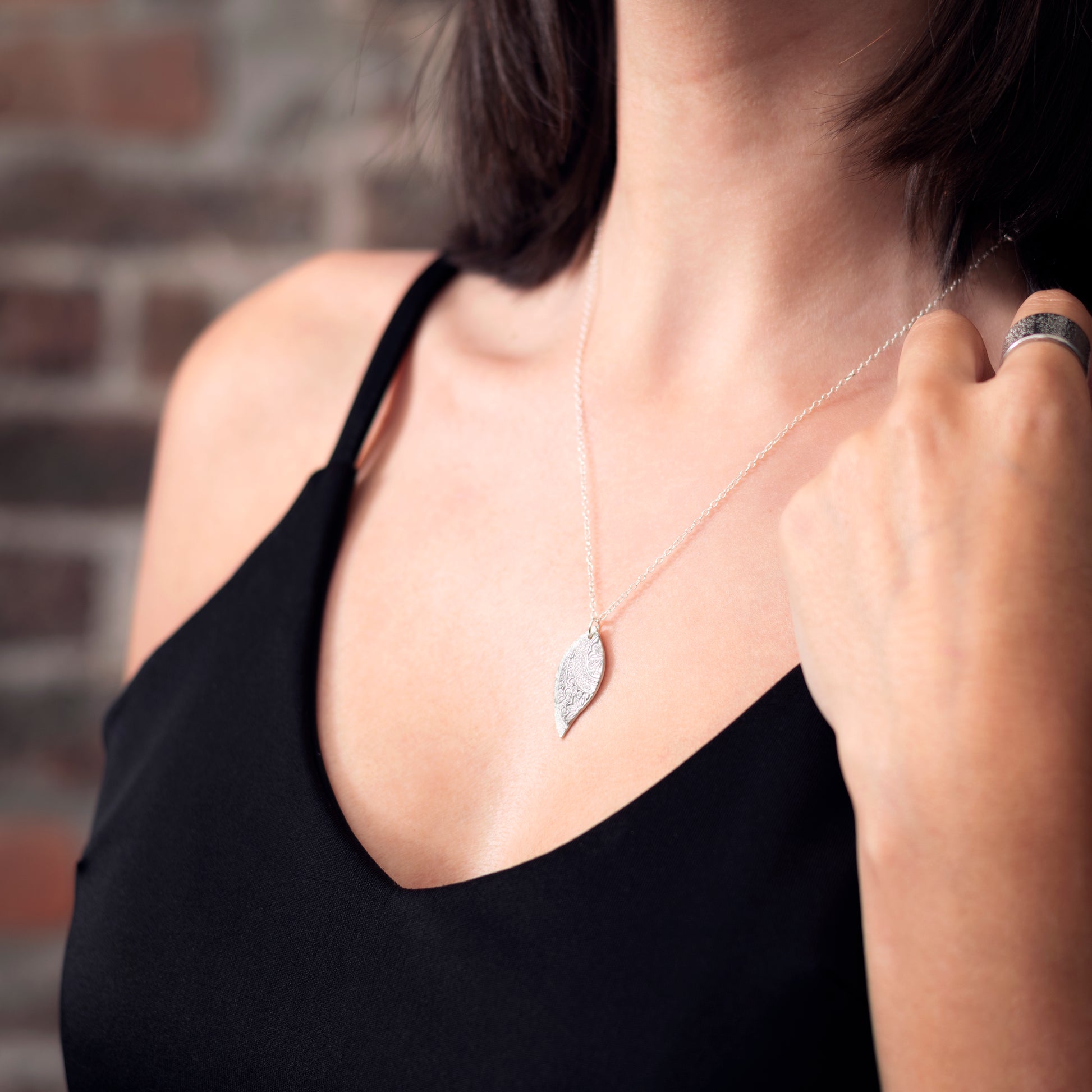 A silver asymmetric patterned leaf-shaped pendant on a chain. Pictured being worn.