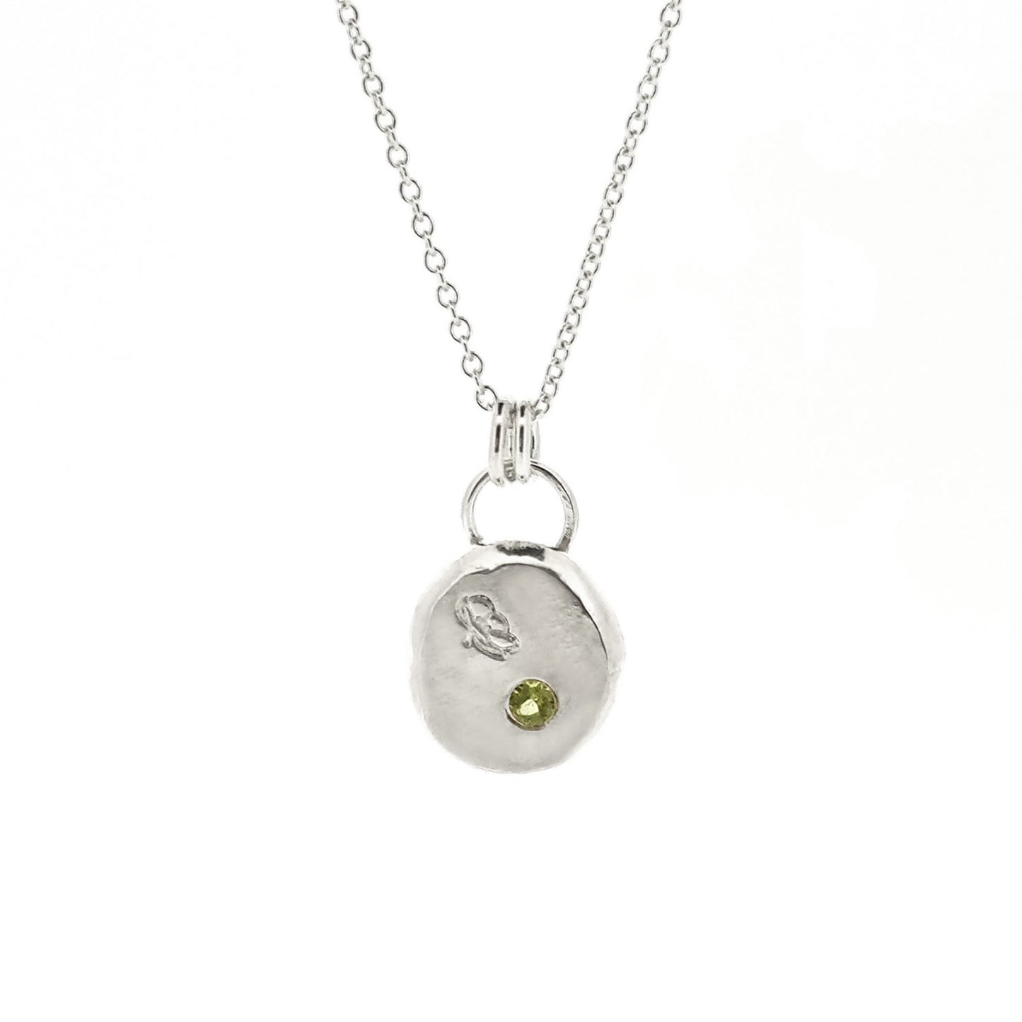 Silver round flat 'pebble' birthstone pendant with a poppy engraved on it and a pale green peridot gemstone on a silver chain. - August