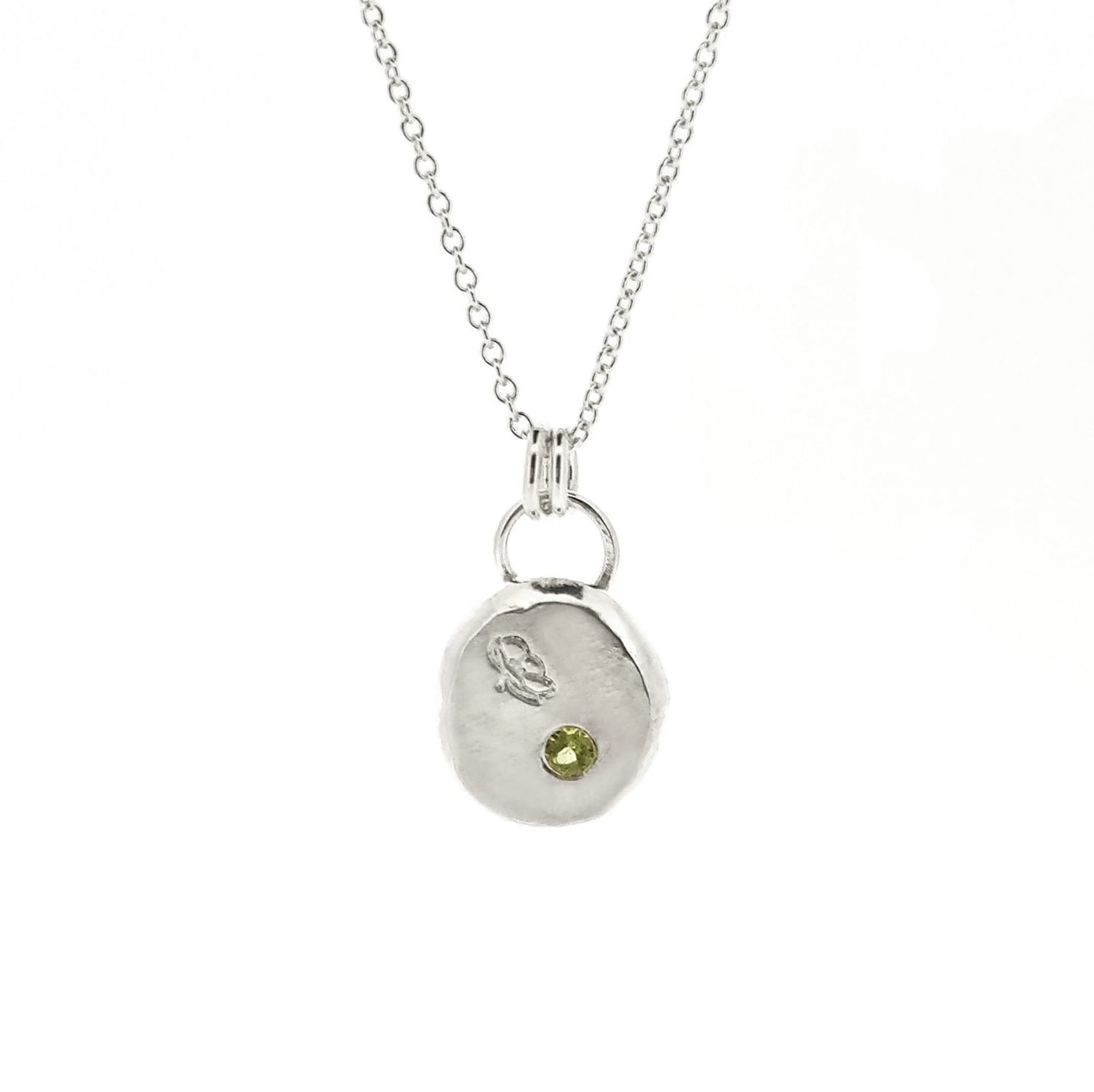 Silver round flat 'pebble' birthstone pendant with a poppy engraved on it and a pale green peridot gemstone on a silver chain. - August