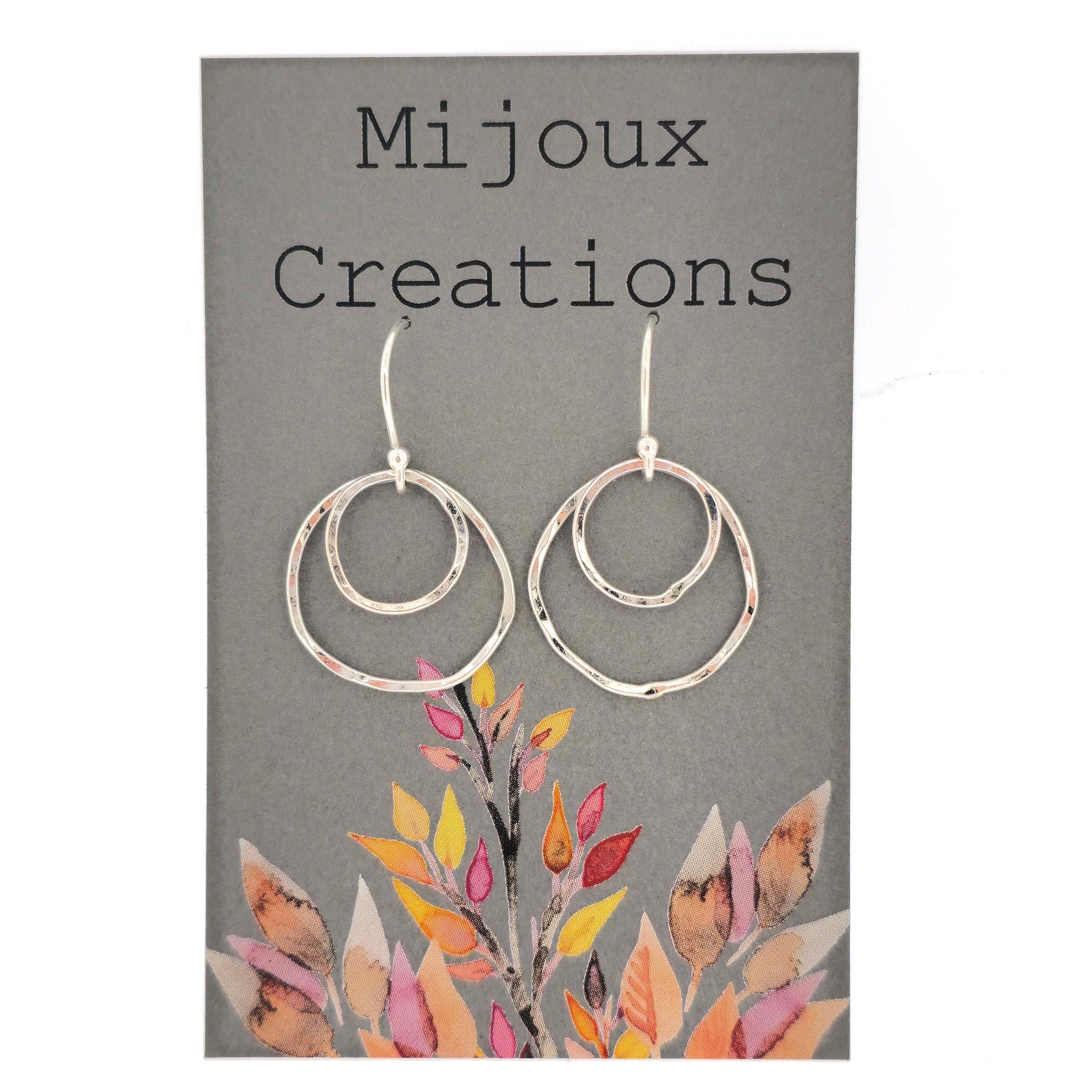 A pair of silver drop earrings. Each earring has 2 rustic circles of different sizes on top of each other with a hammered finish. Displayed on a card.