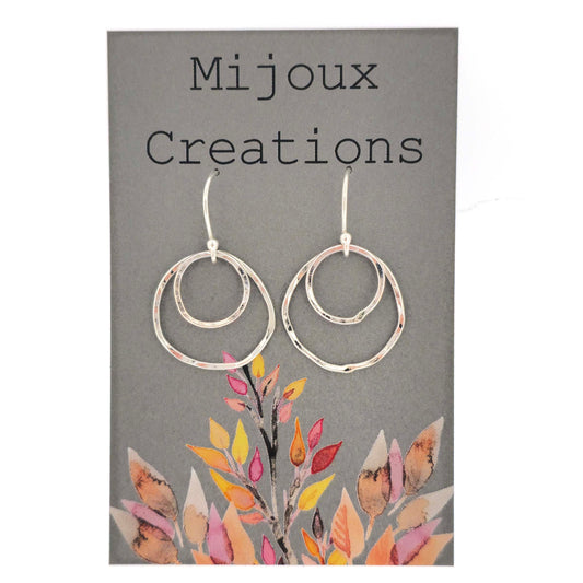 A pair of silver drop earrings. Each earring has 2 rustic circles of different sizes on top of each other with a hammered finish. Displayed on a card.