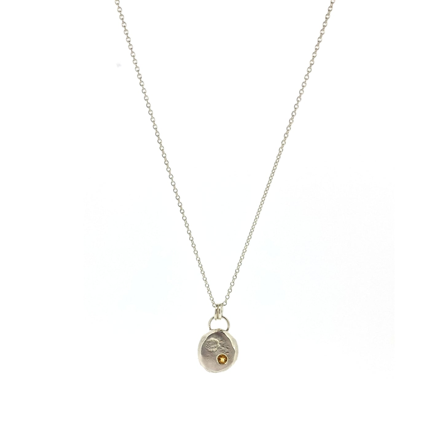 Round silver flat pebble pendant with chrysanthemum flower engraved on it and a flush set yellow citrine gemstone. On a silver chain.