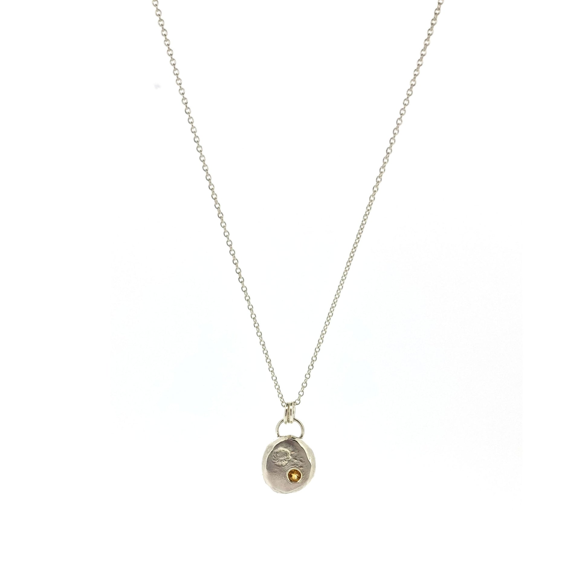Round silver flat pebble pendant with chrysanthemum flower engraved on it and a flush set yellow citrine gemstone. On a silver chain.