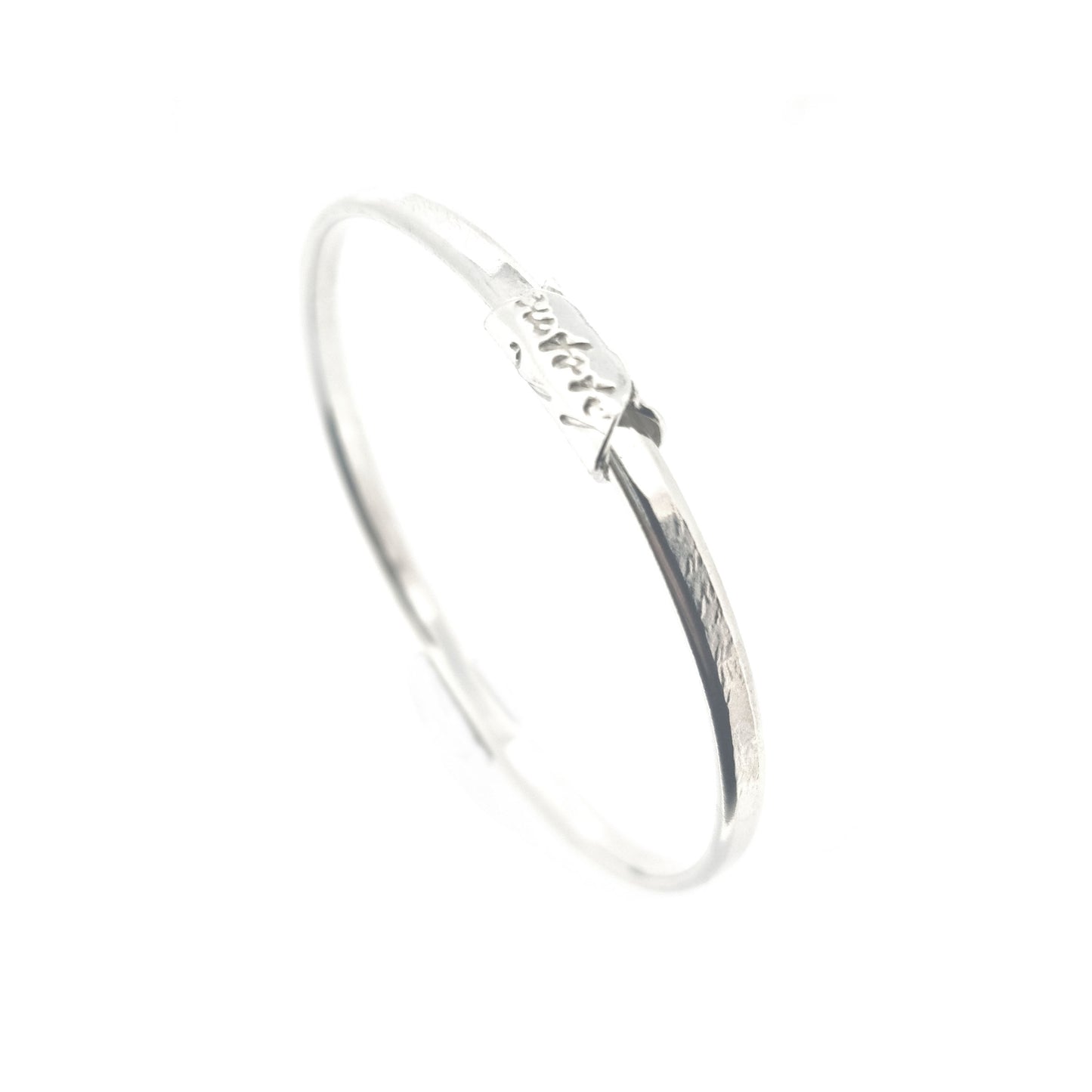 A round silver bangle with an oval profile and a bead with script writing on.