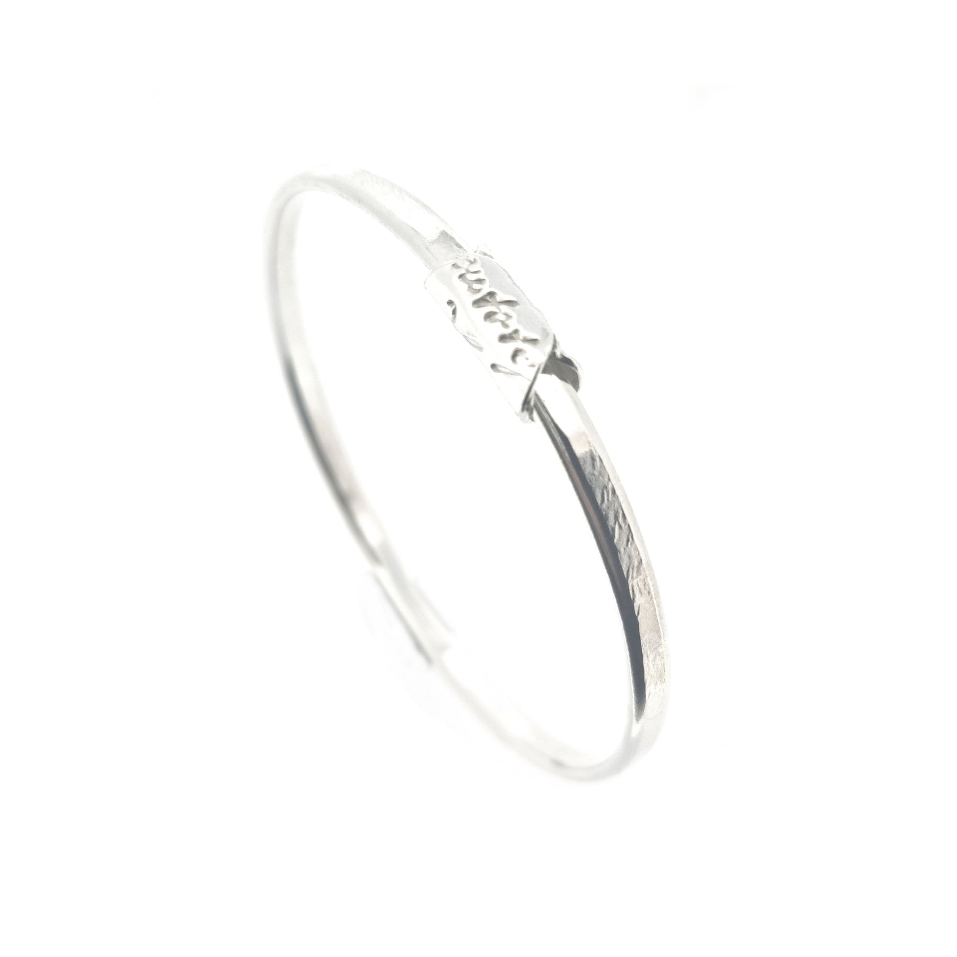 A round silver bangle with an oval profile and a bead with script writing on.