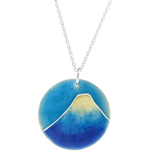 A round silver pendant with a mountain on in blue and white enamels. Suspended on a silver chain.