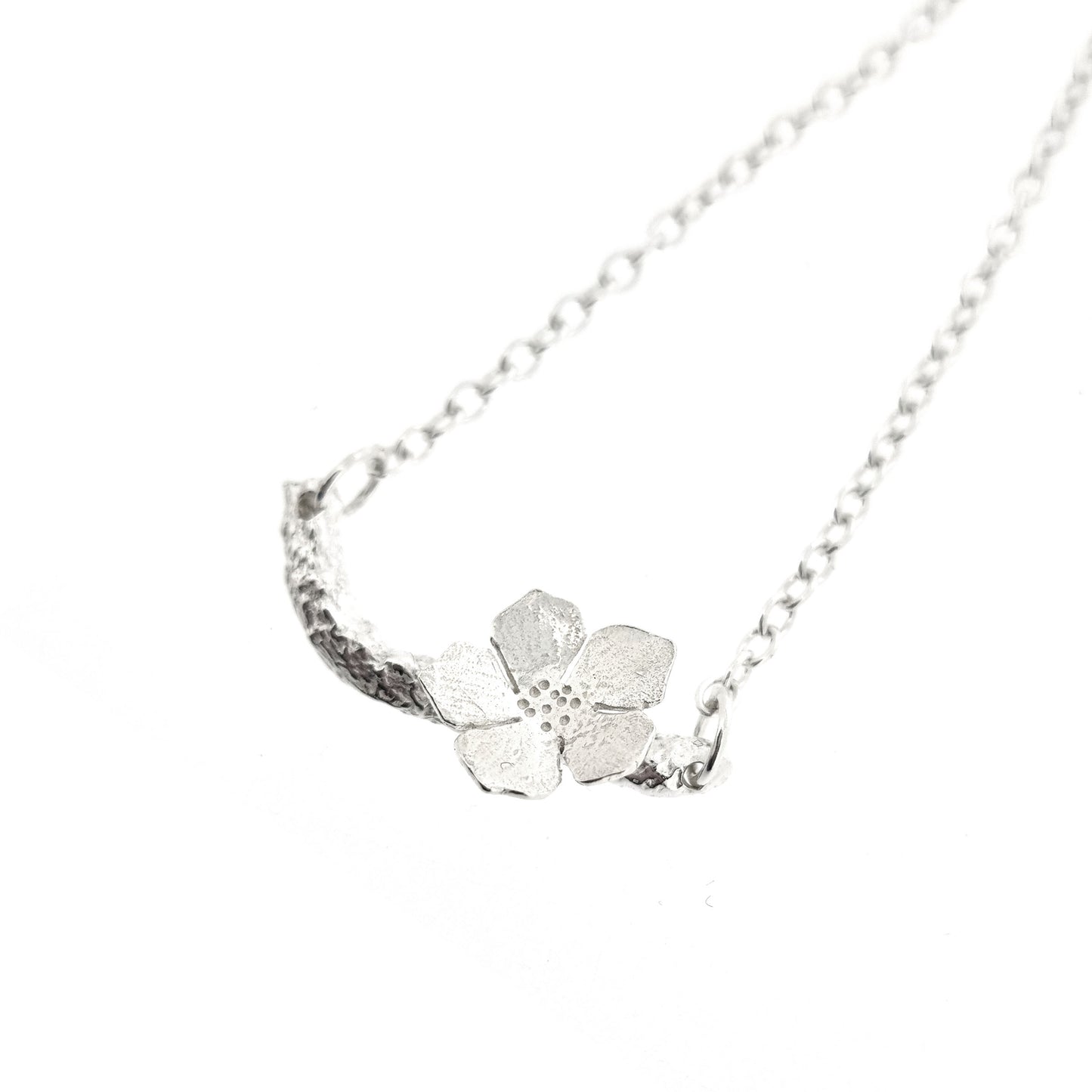 Silver necklace with small branch and a single 5 petal flower on it.