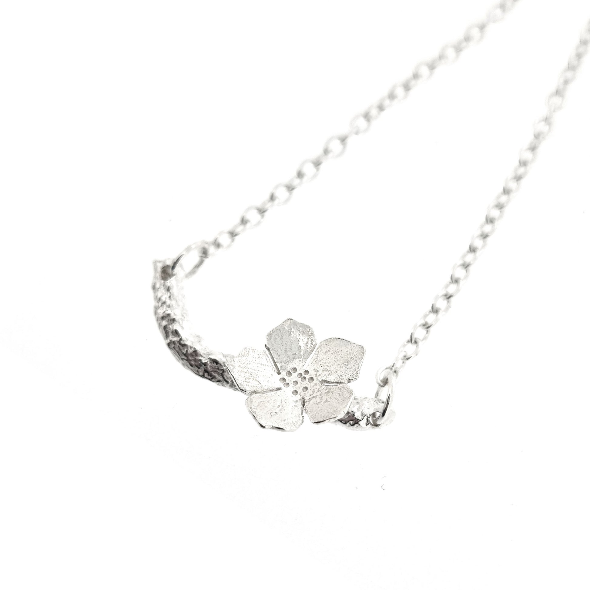 Silver necklace with small branch and a single 5 petal flower on it.