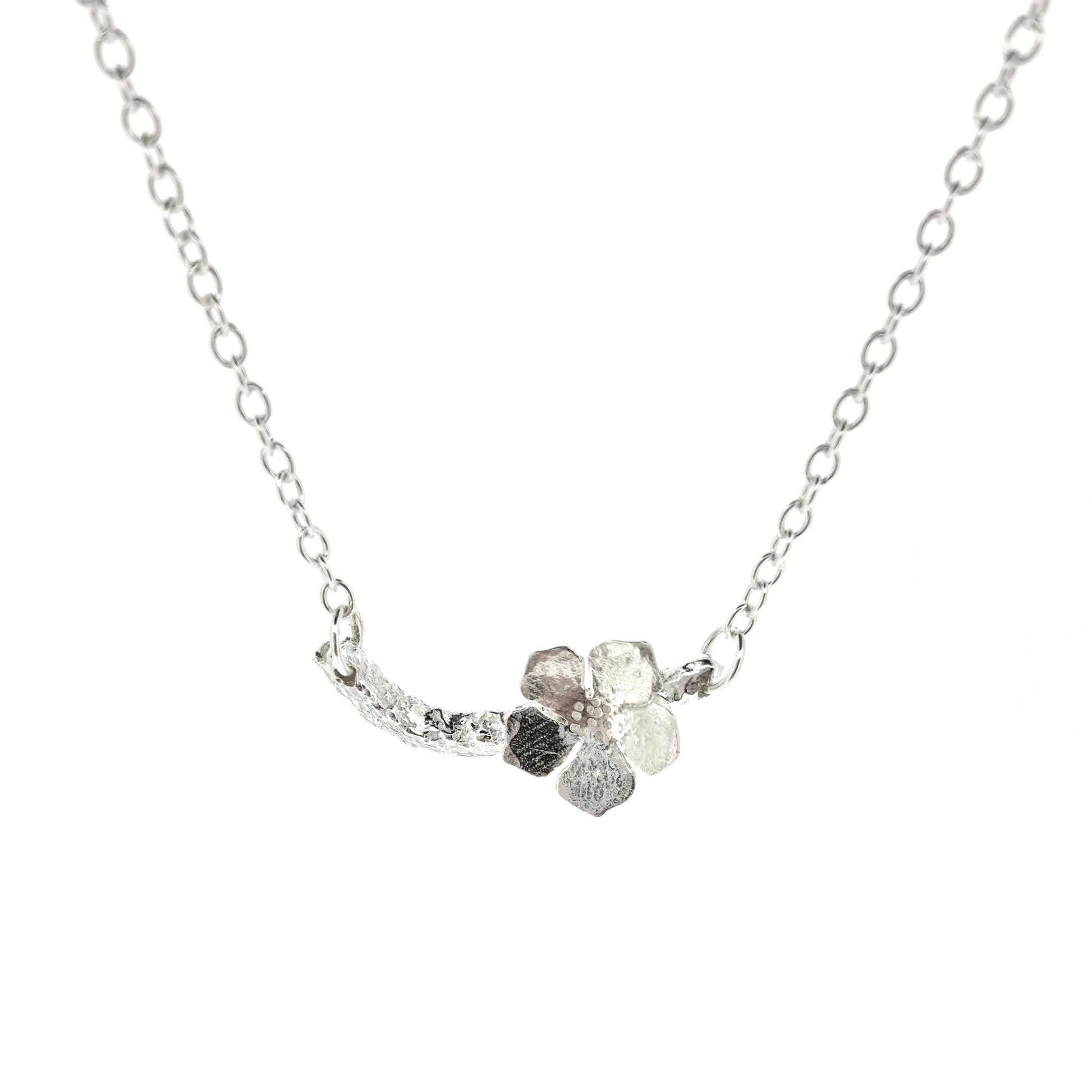 Silver necklace with small branch and a single 5 petal flower on it.