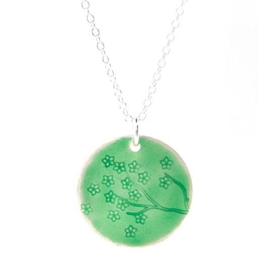 Silver necklace with a round green enamel pendant featuring floral designs on a white background.
