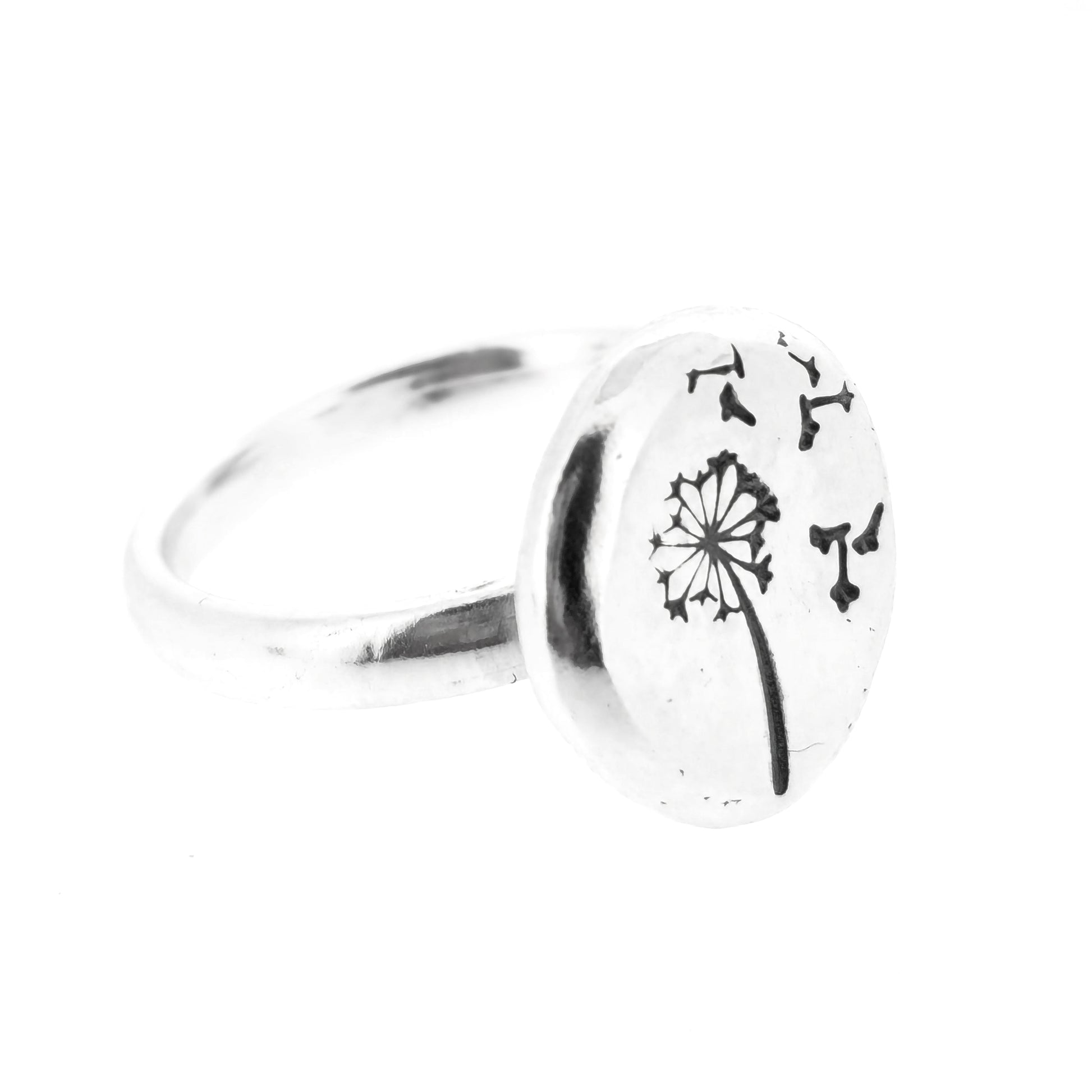 A silver ring with a plain band and a flat pebble top with a dandelion clock and fluff engraved on it.