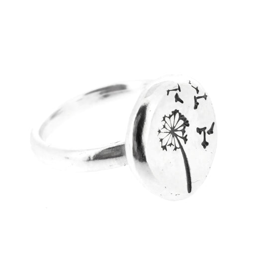A silver ring with a plain band and a flat pebble top with a dandelion clock and fluff engraved on it.