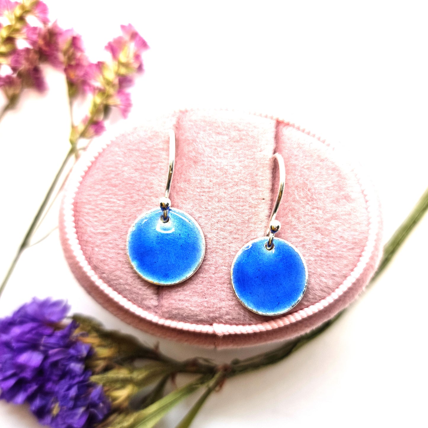 Round silver drop earrings with dark blue enamel. Shown in jewellery box with flowers.