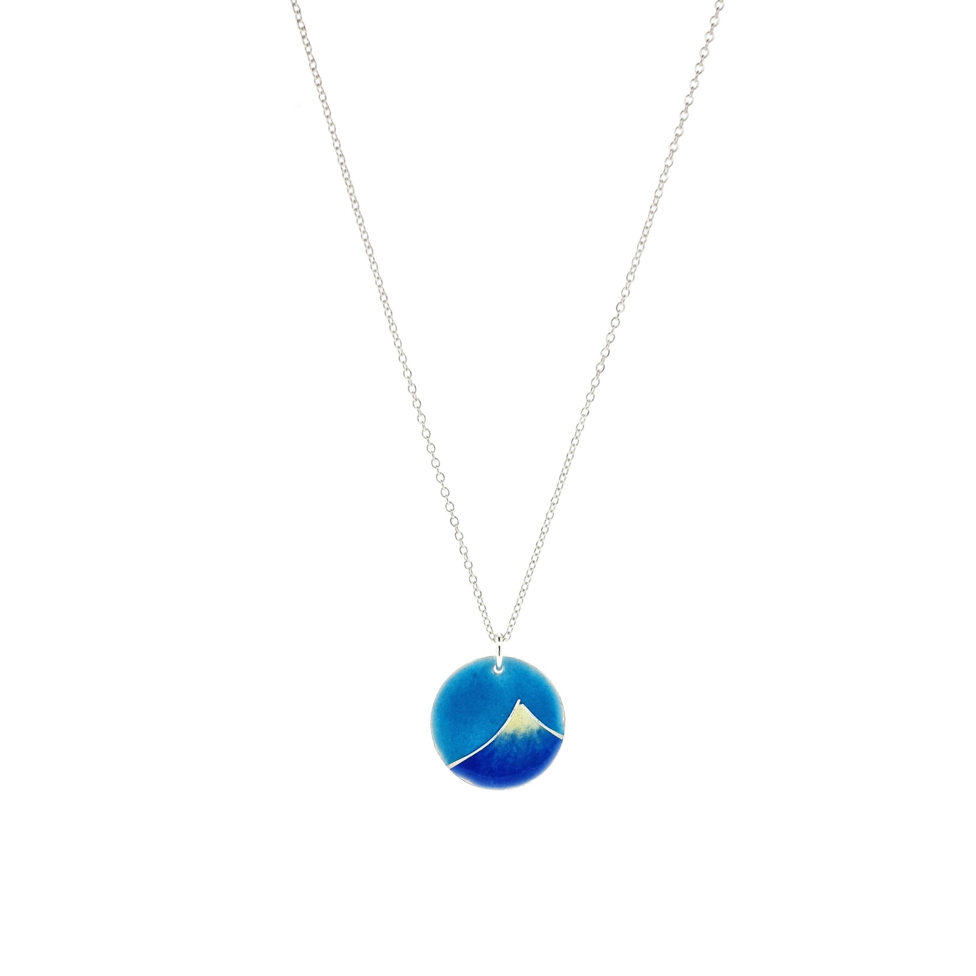 Silver and enamel round pendant featuring a dark blue and white mountain with a turquoise blue sky. On a silver chain.