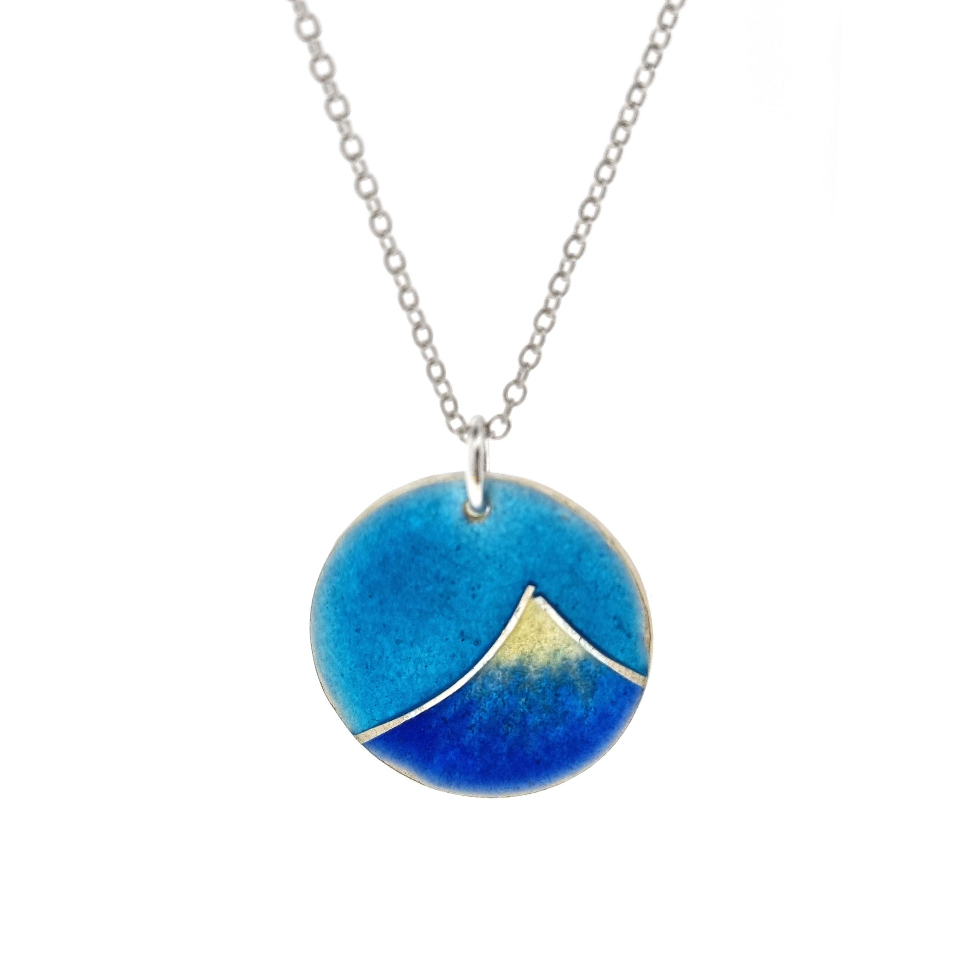 Silver and enamel round pendant featuring a dark blue and white mountain with a turquoise blue sky. On a silver chain.