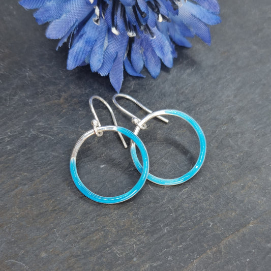 Silver open circle drop earrings with turquoise blue enamel. Shown with blue flower.