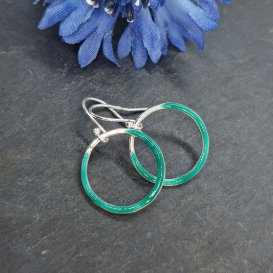 Silver open circle drop earrings with turquoise green enamel. Shown with blue flower.