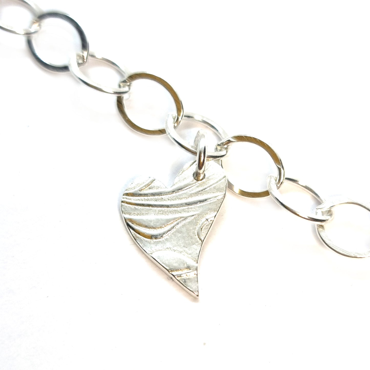 Silver large link chain bracelet with asymmetrical patterned heart charm.