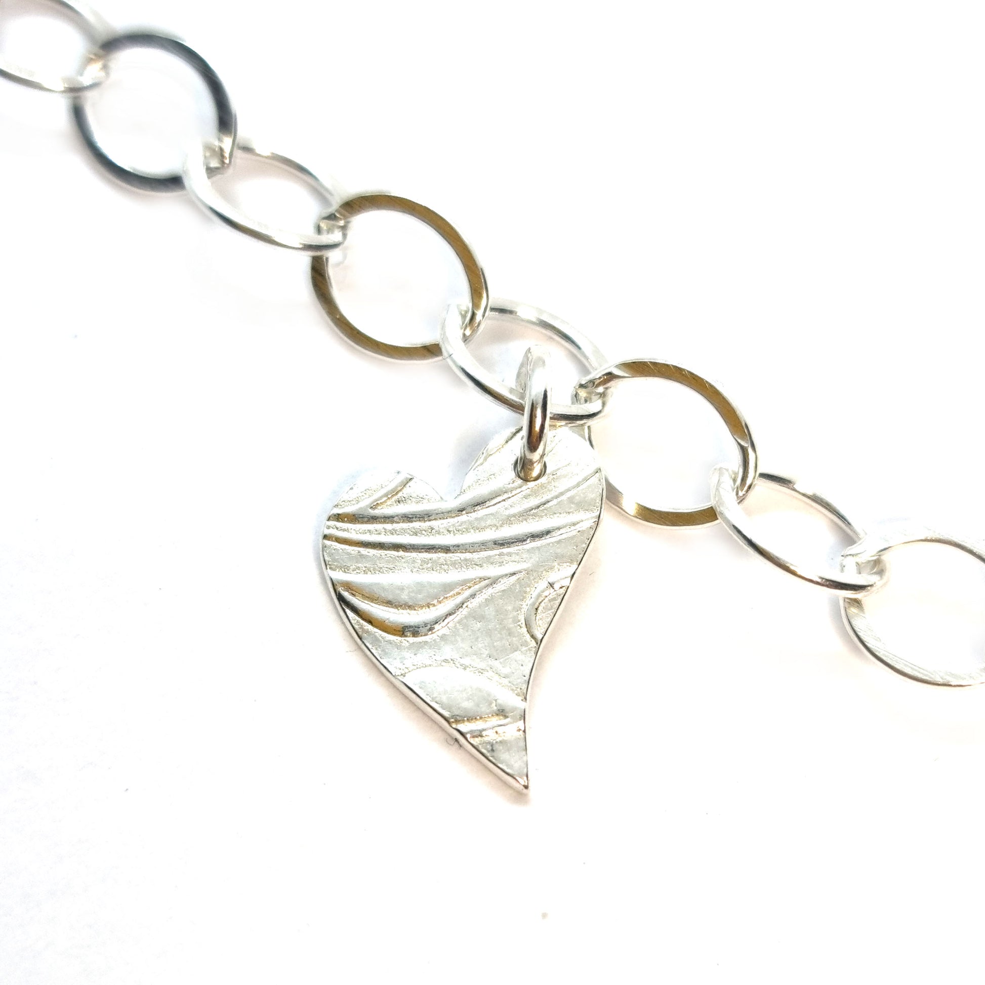 Silver large link chain bracelet with asymmetrical patterned heart charm.