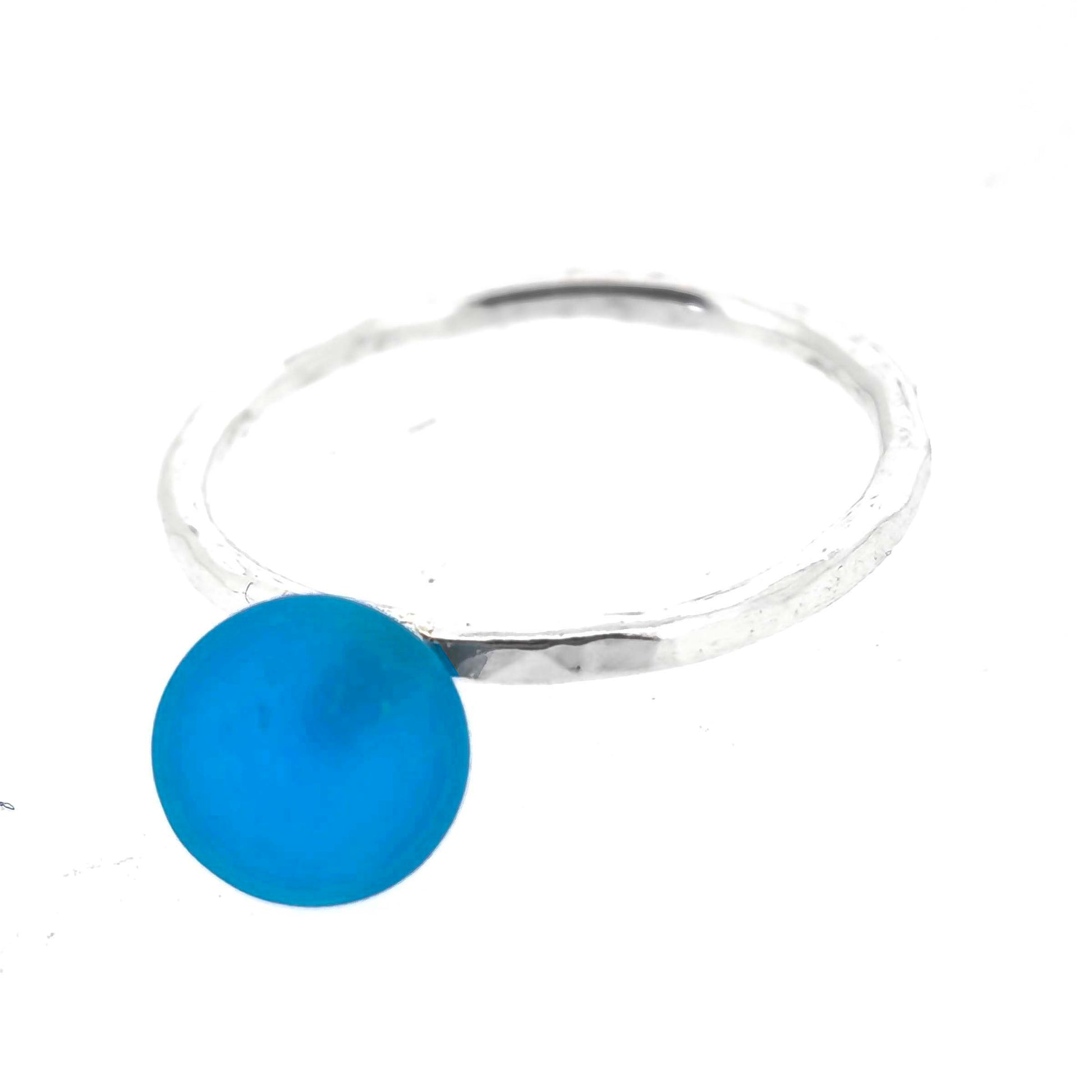 A silver ring with a thin band with a hammered finish and a bright blue glass sphere on top. Mijoux Creations.