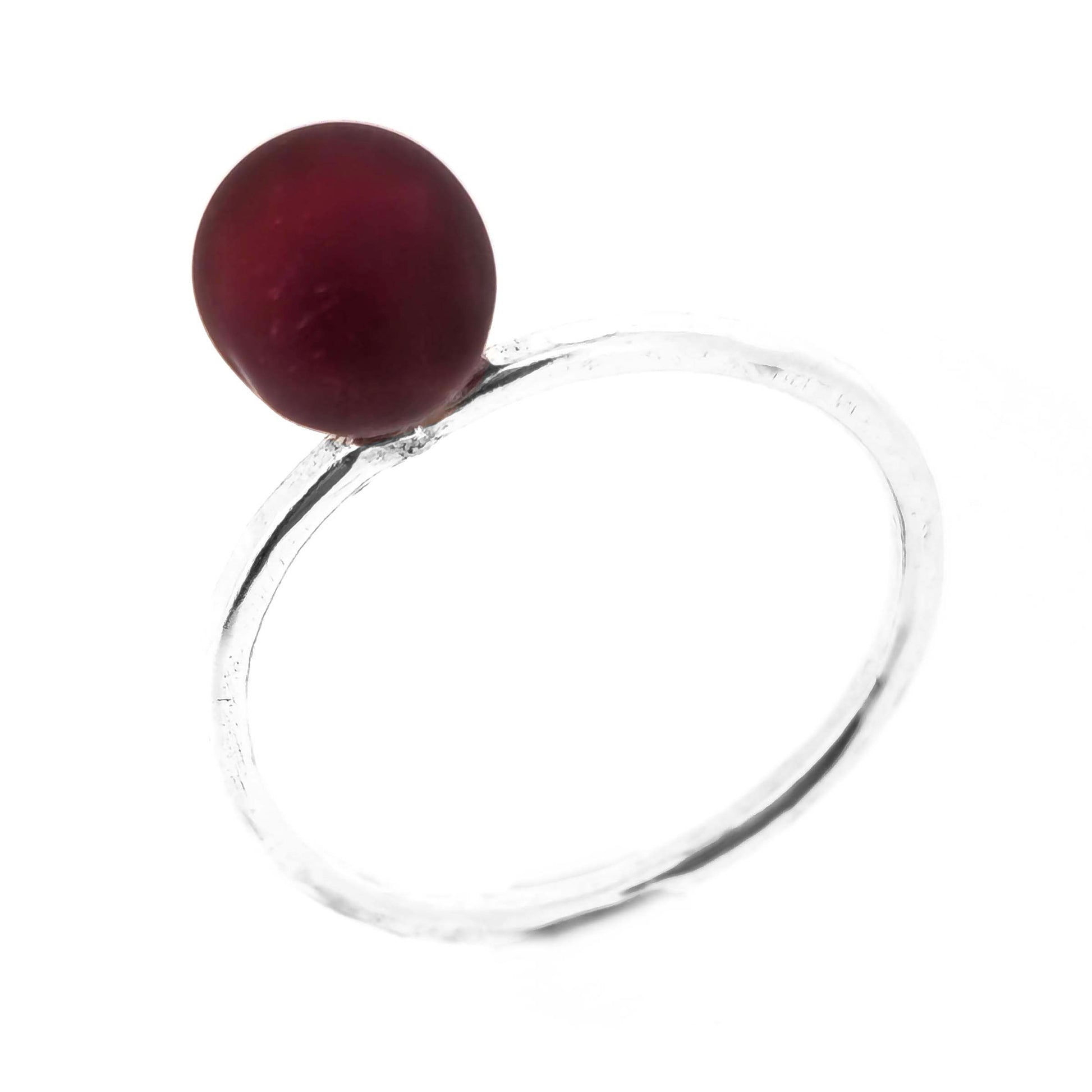 A silver ring with a thin band with a hammered finish and a dark red glass sphere on top.