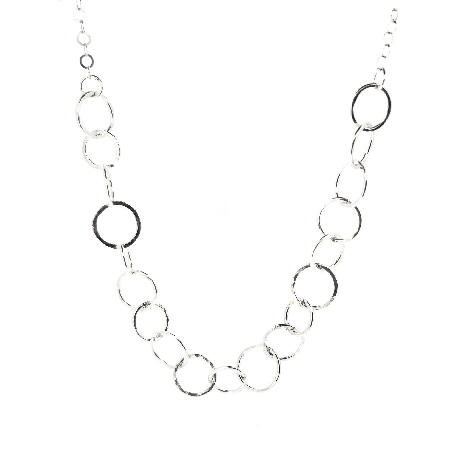 A silver necklace made up of different size circles with a hammered finish and smaller silver chain at the back.