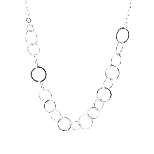 A silver necklace made up of different size circles with a hammered finish and smaller silver chain at the back.