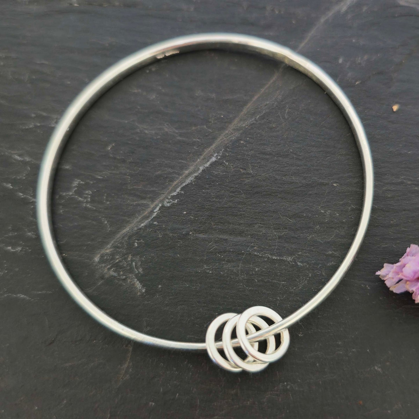 Silver textured bangle with 3 circle beads on a dark slate background with flowers