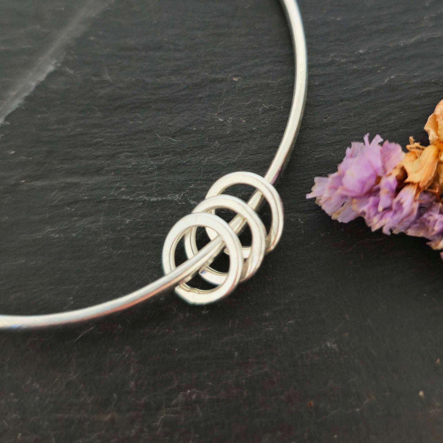 Section of a silver textured bangle with 3 circle beads on a dark slate background with flowers