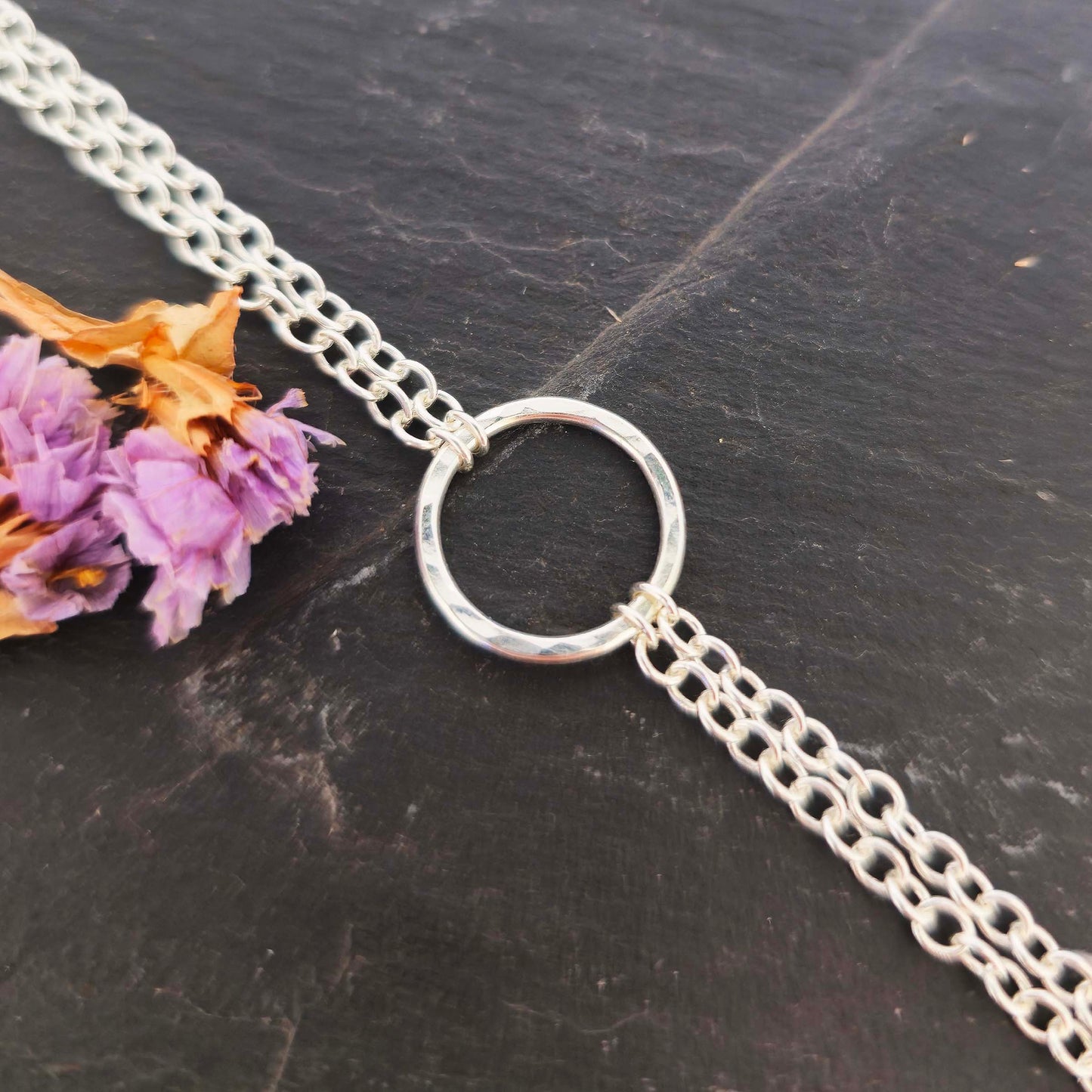 Silver double chain bracelet with a central hammered circle on a slate background with dried flowers